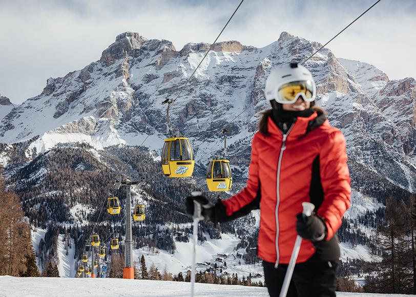 Sciatrice sulle piste con cabinovia e Dolomiti innevate sullo sfondo